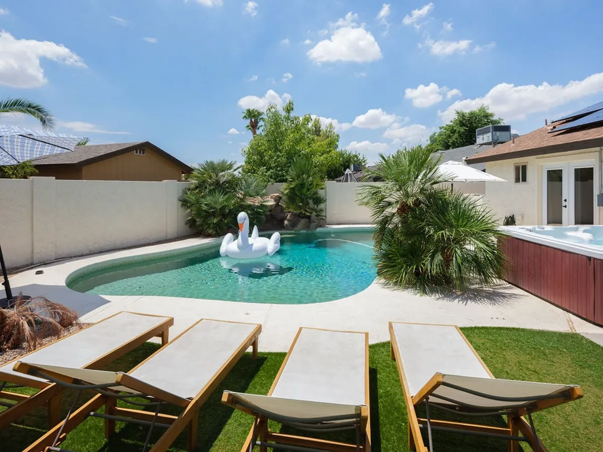 An inviting backyard scene featuring a sparkling swimming pool with a playful swan float, surrounded by lounge chairs and lush greenery. The setup evokes a lively, resort-like atmosphere perfect for group relaxation and social gatherings.