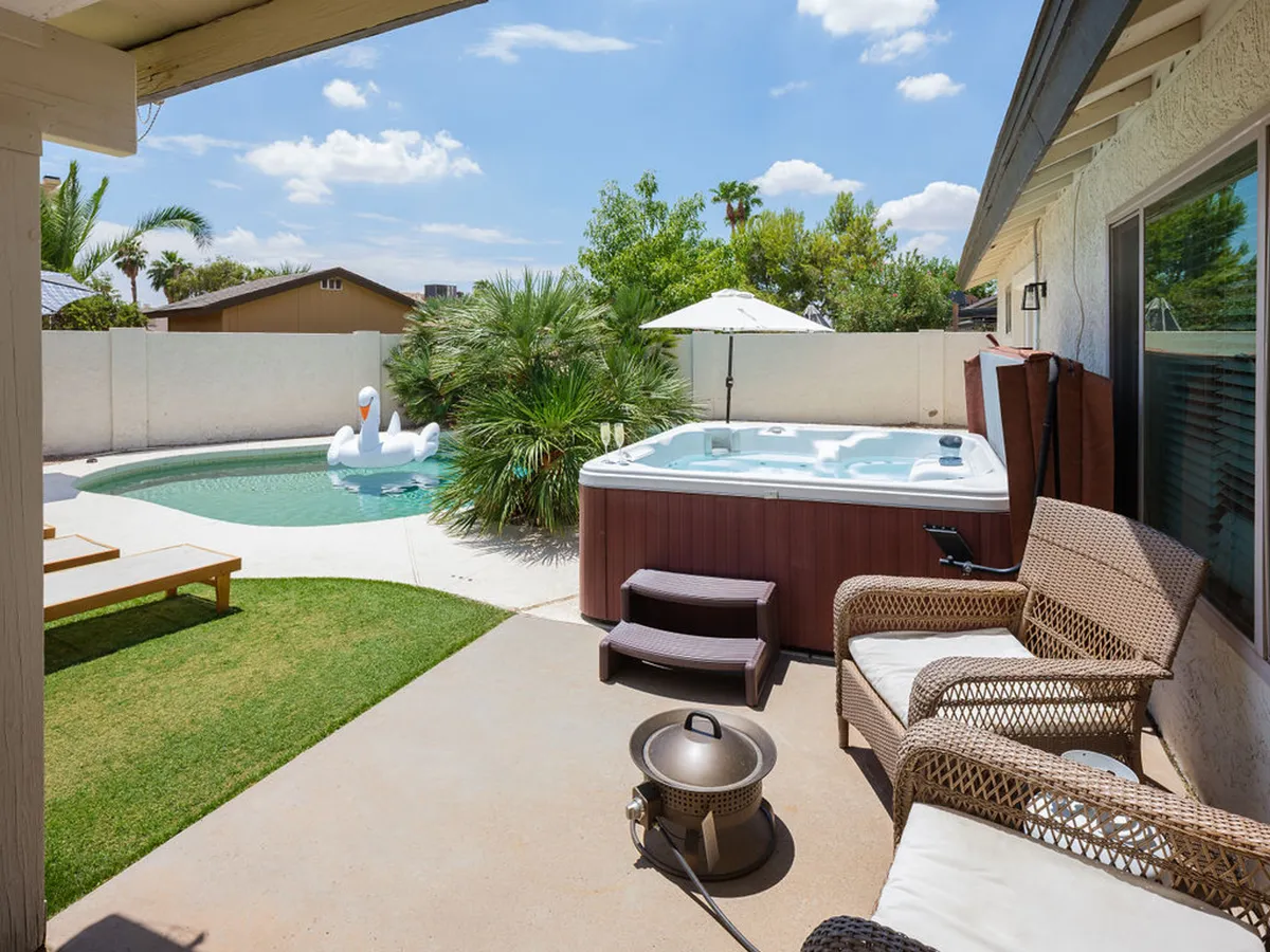 An inviting outdoor living area with a hot tub, swimming pool, spacious lawn, and comfortable seating under an umbrella. The space is set up for socializing, relaxing after a day on the course, or gathering for a barbecue with friends.