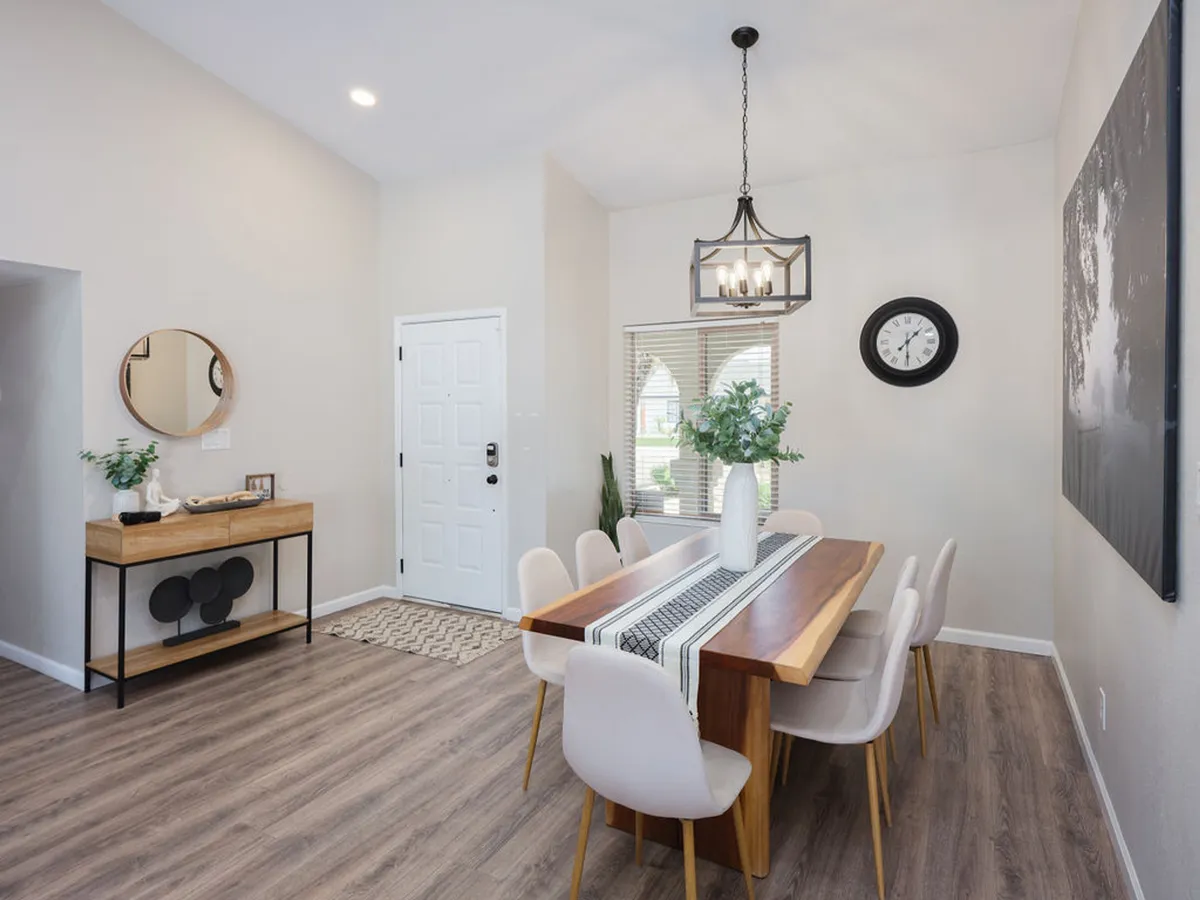 A cozy dining area centered on a large table, complemented by an elegant hanging light fixture, a mirror, and an inviting entrance. The ambiance suggests a space designed for memorable gatherings, family dinners, or festive celebrations.