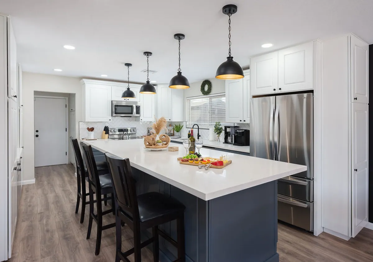 A spacious, modern kitchen featuring a central island with pendant lights, sleek stainless steel appliances, and touches of decorative greenery. The layout is ideal for cooking, socializing, and family gatherings, emphasizing a contemporary, inviting atmosphere.