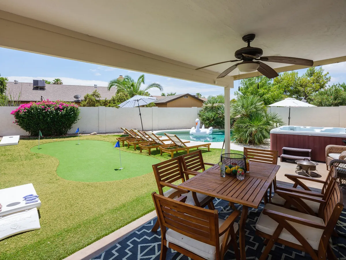 A well-appointed outdoor living area with a dining table set beside a sparkling swimming pool, sun loungers, a hot tub, and a putting green. The arrangement encourages both group activities and quiet relaxation, with ample space for dining, swimming, and enjoying the sunshine.