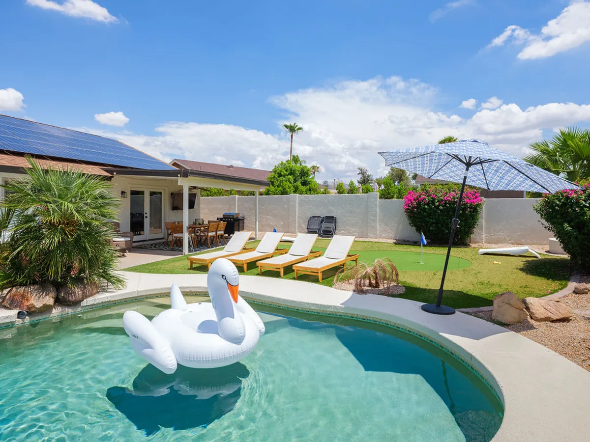 The hero image features a sparkling swimming pool at sunset, with an inviting inflatable swan floating on the water. Surrounding the pool are chic lounge chairs and an umbrella for shade, as well as an outdoor dining area perfect for enjoying meals or drinks al fresco. The setting is festive and relaxed, signaling a space ideal for sunbathing, swimming, and gathering with friends or family.
