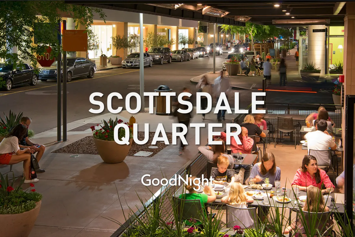 A vibrant exterior view of an outdoor dining area with people enjoying their meals, surrounded by shops and glowing ambient lighting, located along a lively street with parked cars. The mood is energetic and inviting, capturing the experience of local dining and exploration.