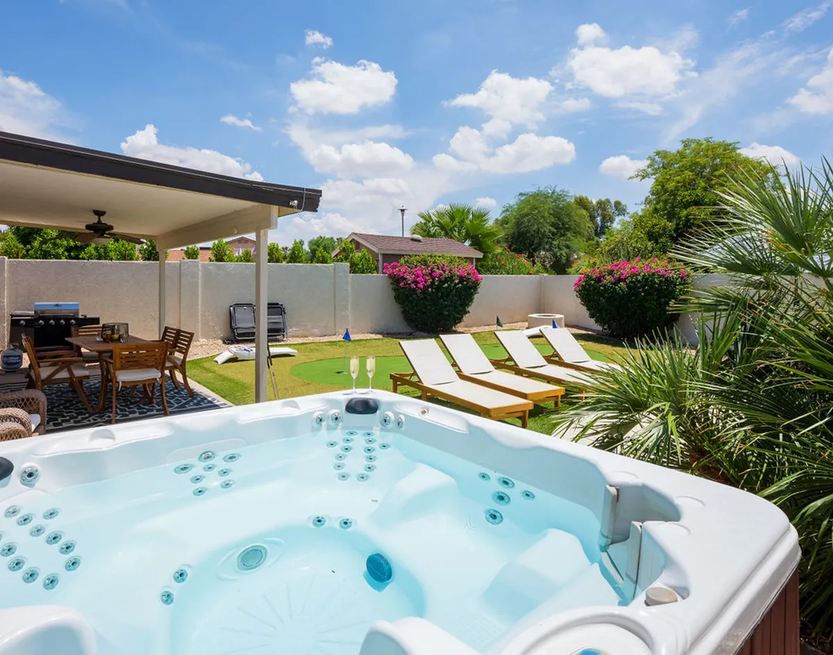A beautifully landscaped backyard with a bubbling hot tub, ample outdoor seating, lounge chairs, and lush, flowering shrubs. The scene is tranquil yet ideal for hosting friends or unwinding after a day out.