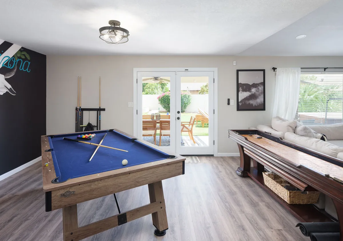 A cozy game area centered around a sleek pool table, complemented by a sofa and accented with French doors that allow natural light to flood the space. Tasteful wall art adds a playful yet sophisticated touch, while the overall mood is friendly and inviting.