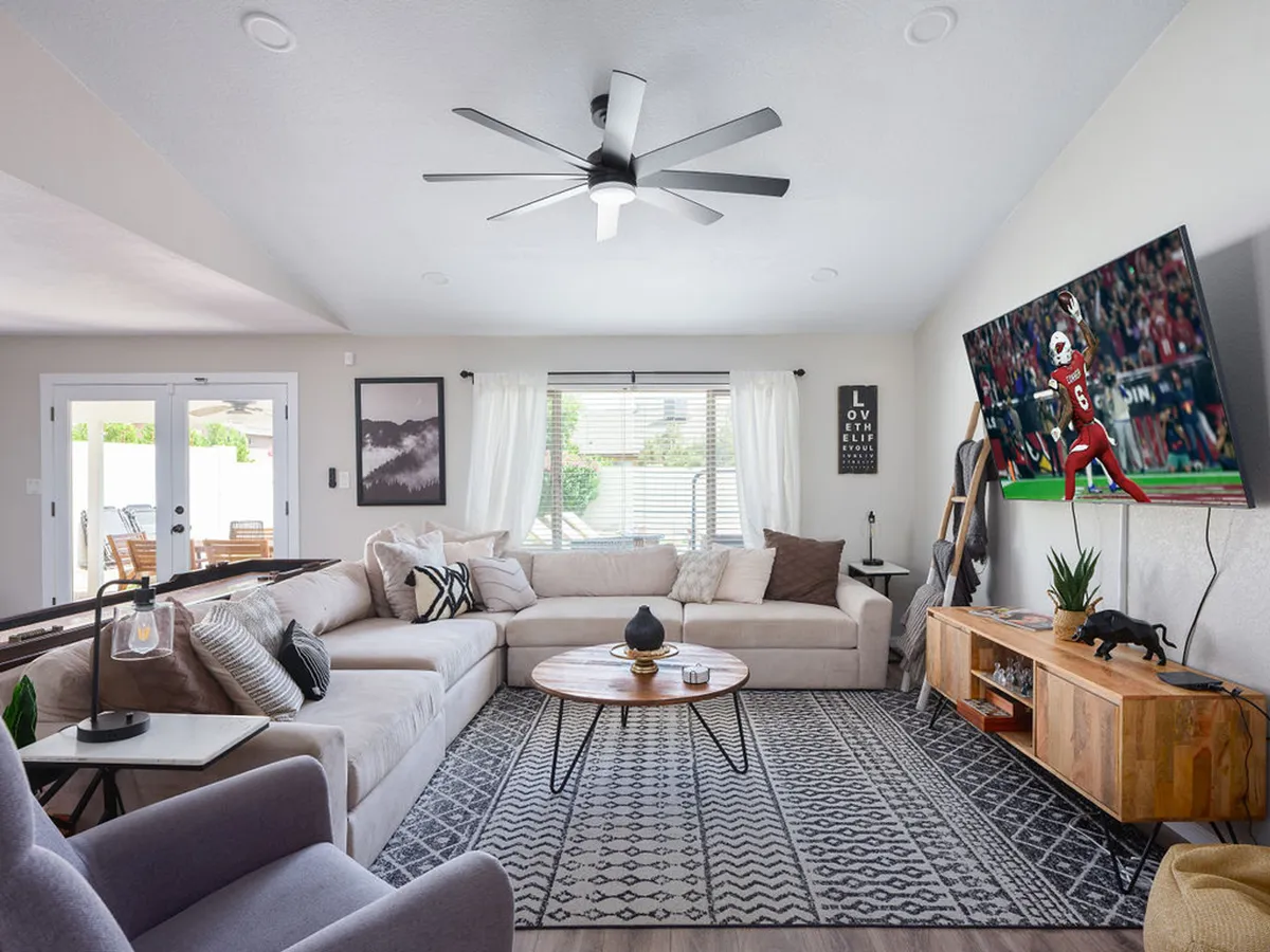 A lively living room highlighted by a large sectional sofa, a round coffee table, and a television displaying a football game. Decorative wall art adds character, and the arrangement suggests a perfect setup for both sports viewing parties and family movie nights.
